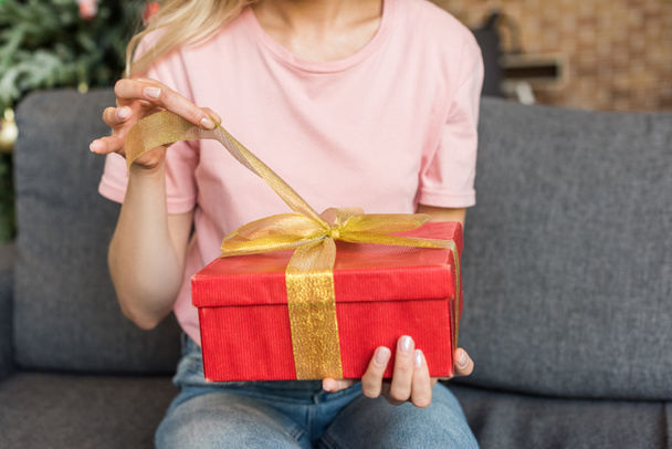 Schnappschuss einer jungen Frau, die auf Sofa sitzt und Weihnachtsgeschenk öffnet - Foto, Bild