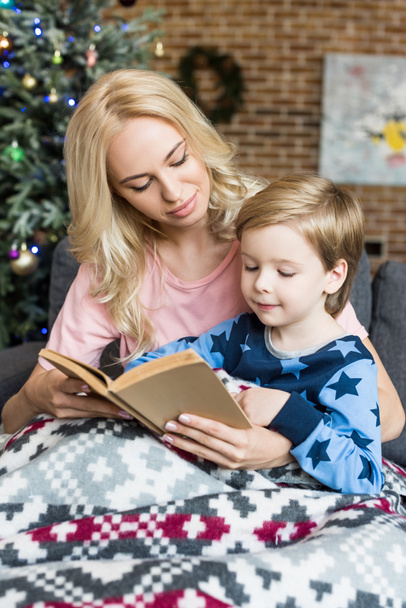 hermosa joven madre y adorable pequeño hijo leyendo libro juntos en Navidad
   - Foto, imagen