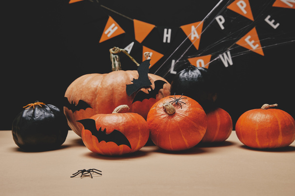 оранжевые и черные тыквы, бумажные летучие мыши и бумажные гирлянды со словами счастливого Хэллоуина
 - Фото, изображение