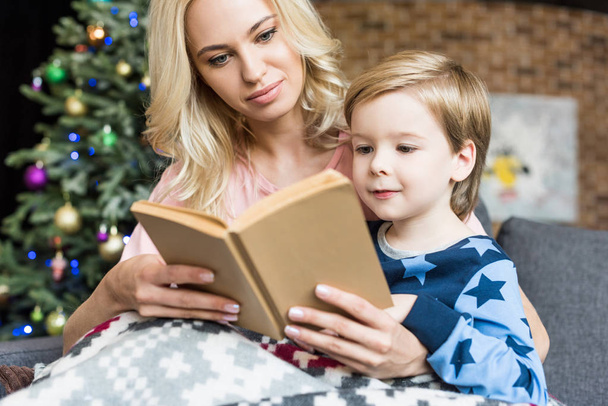 mother and cute little son reading book together at christmas time  - Photo, Image