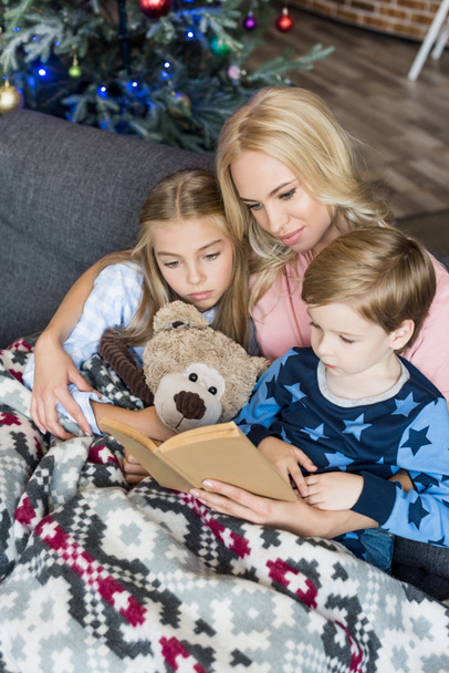 high angle view of mother reading book with cute kids in pajamas at christmas time  - Photo, Image