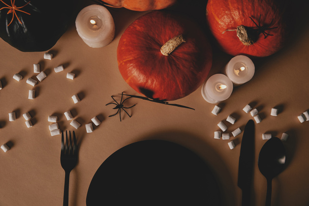 top view of pumpkins, black plate, fork and knife with marshmallows on table, halloween concept - Foto, Imagem