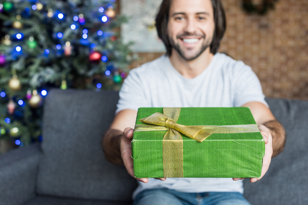 happy young man holding christmas present and smiling at camera - Fotoğraf, Görsel