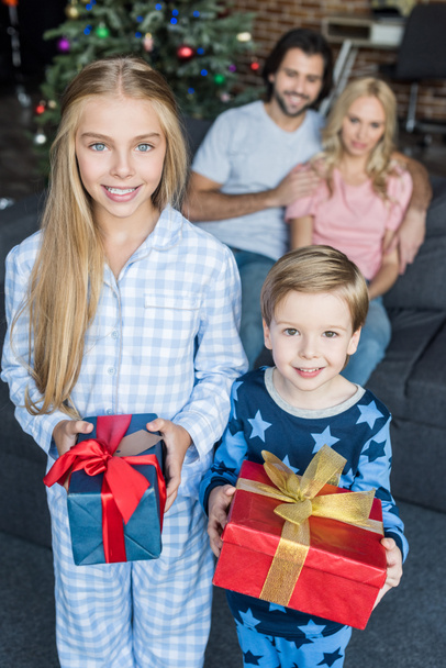 vista de ángulo alto de niños felices en pijama sosteniendo regalos de Navidad mientras los padres se sientan detrás
 - Foto, Imagen