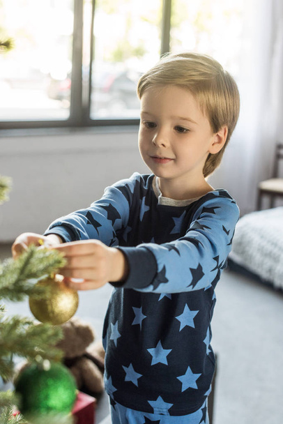 cute smiling little boy in pajamas decorating christmas tree - Photo, Image