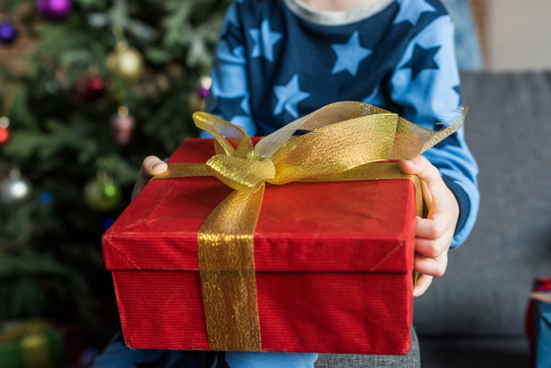gyerek pizsama ül a kanapén, és a gazdaság karácsonyi ajándékot részleges kiadványról - Fotó, kép