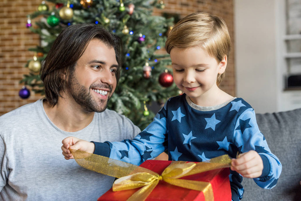 happy father looking at adorable little son opening christmas gift - Foto, Bild