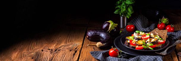 Eggplant grilled with aromatic feta cheese and tomatoes on black plate - Foto, Imagen