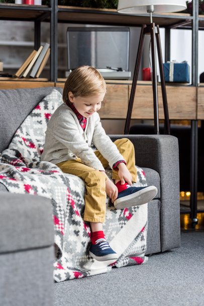 cute happy child sitting on couch and putting on shoe - Valokuva, kuva