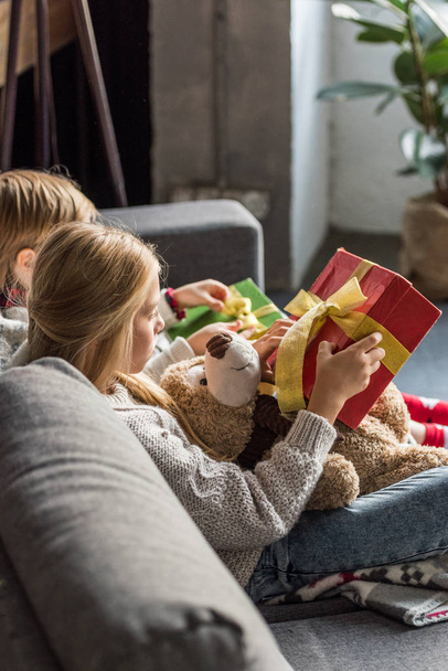 side view of children sitting on couch and opening christmas gifts - Foto, Bild