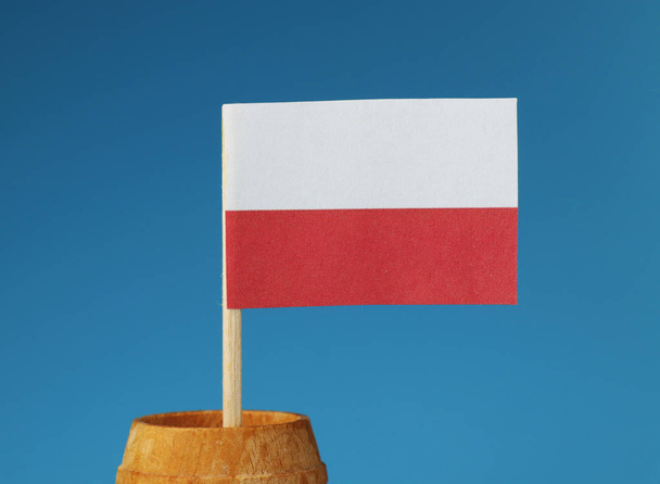Un détail sur le drapeau national de la pologne sur bâton en bois dans un tonneau en bois sur fond bleu
 - Photo, image