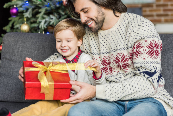 Gelukkig vader kijken schattig zoontje openen kerstcadeau  - Foto, afbeelding