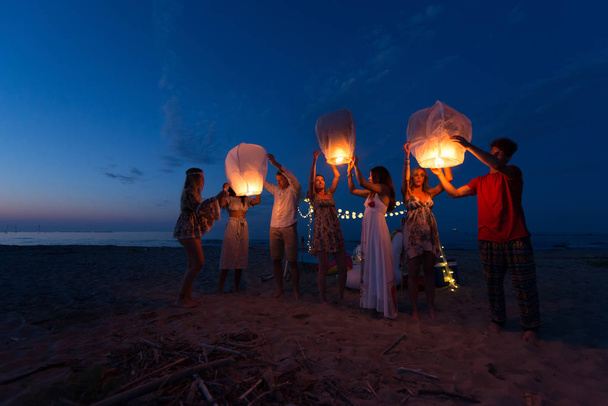 Milenials jóvenes sosteniendo y encendiendo la linterna del cielo - Festival de la linterna en la playa
 - Foto, imagen