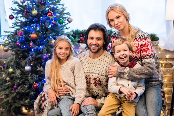 familia feliz en hermosos suéteres abrazando y sonriendo a la cámara en Navidad
 - Foto, Imagen
