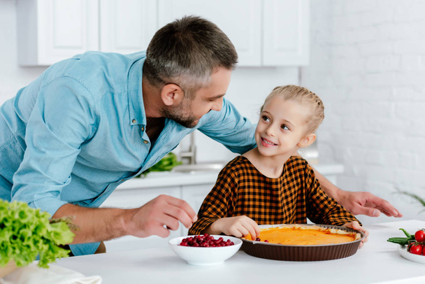 счастливый отец и очаровательная маленькая дочь украшают тыквенный пирог на День Благодарения вместе
 - Фото, изображение
