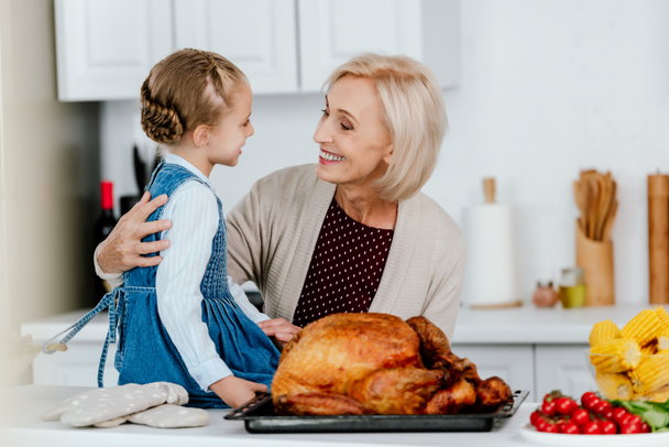 smiling mature woman preparing thanksgiving turkey with granddaughter - Photo, Image