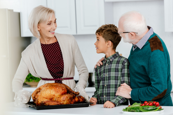 excited little kid with grandparents preparing thanksgiving turkey together at kitchen - Foto, Imagen