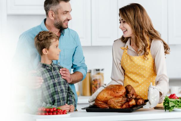 adorable little kid with parents preparing thanksgiving turkey together at kitchen - Foto, Imagem