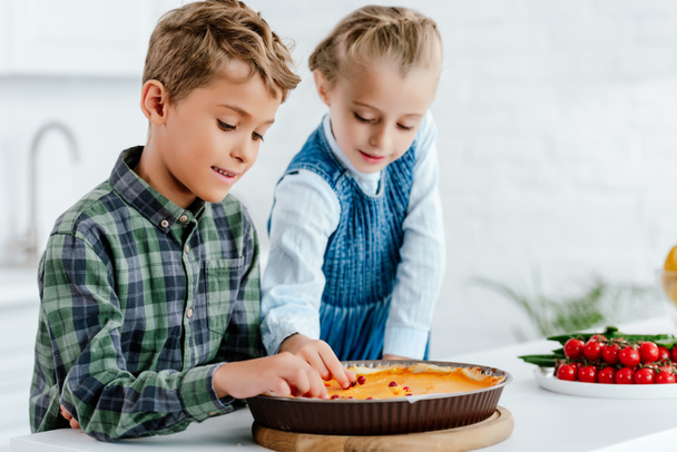 adorable siblings decorating pumpking pie with berries together at kitchen - Photo, Image