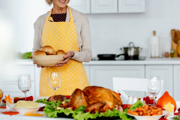 przycięte zdjęcie uśmiechnięta kobieta gospodarstwa miska z chlebem w pobliżu służył tabeli na Święto Dziękczynienia  - Zdjęcie, obraz
