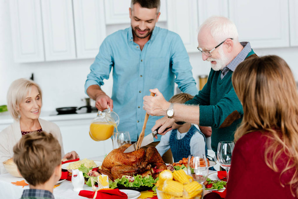 grandfather slicing baked turkey at served table while family celebrating thanksgiving  - Foto, Bild