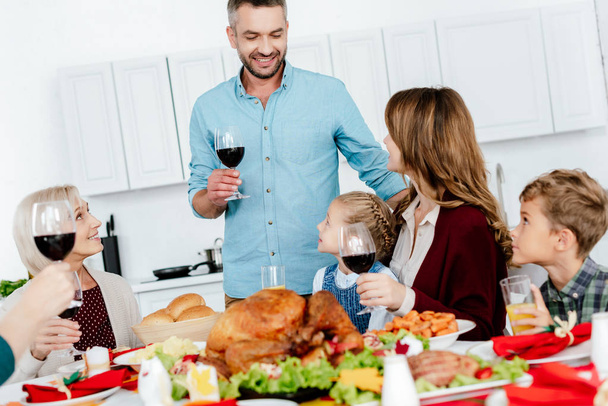 happy adult man with wine glass making toast at served table with turkey while his family celebrating thanksgiving  - Photo, Image