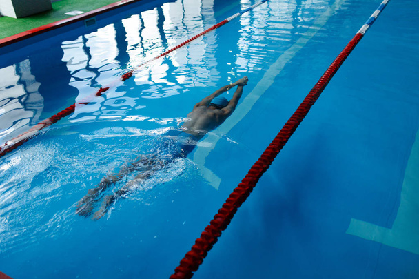 Photo on top of athlete man in blue cap swimming on path in pool under water - Foto, Imagem