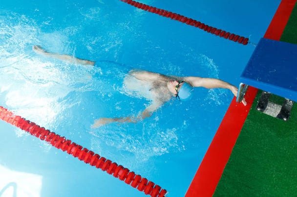 Photo on top of athlete man in blue cap swimming on back in swimming pool - Fotoğraf, Görsel