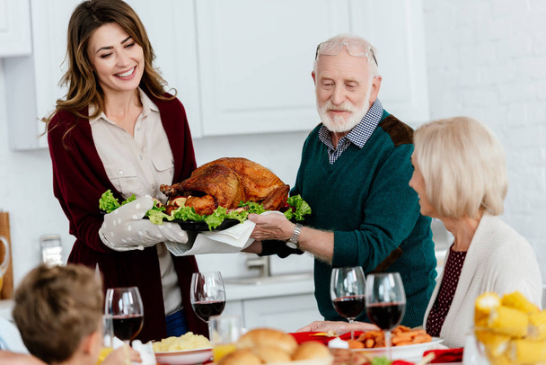 senior man and adult woman carrying baked turkey for thanksgiving dinner with family at home  - Foto, Bild