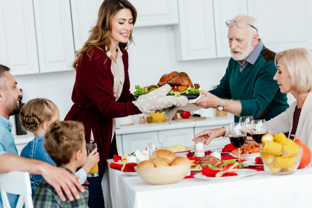 smiling adult woman and senior man carrying baked turkey for thanksgiving dinner with family  - Фото, зображення