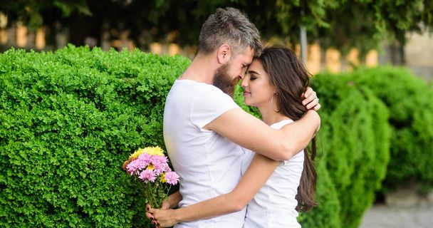 Couple in love hugs on date in park green bushes background. Man fall in love with gorgeous girl. Man bearded hipster hugs woman. Strong romantic feelings become true love. He will never let her go - Photo, image