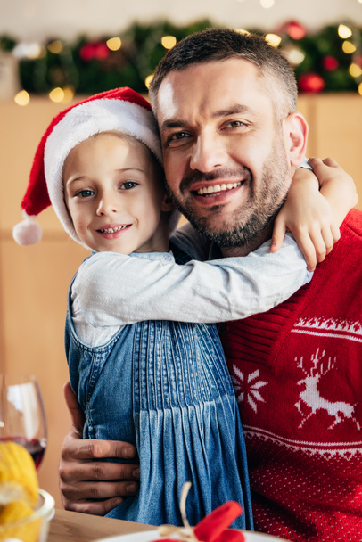 portrait de heureux petit enfant à Noël embrassant père à table avec dîner de vacances
  - Photo, image