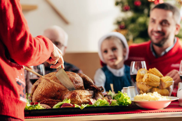 imagen recortada de mujer rebanando delicioso tukey para la cena de Navidad con la familia feliz en casa
 - Foto, Imagen