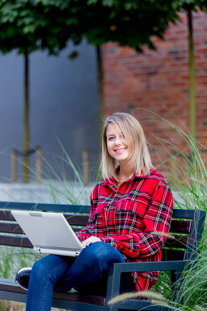 Portrait of young woman with notebook sitting on bench near house.  - Photo, Image