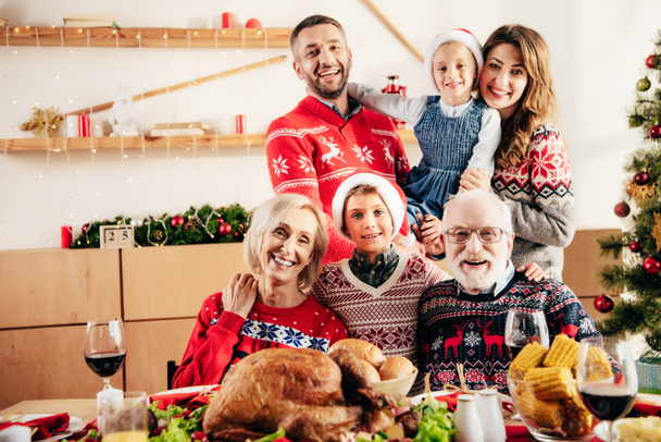 onnellinen perhe pikkulasten kanssa jouluhatuissa istuu pöydässä jouluaterian aikana kotona
 - Valokuva, kuva