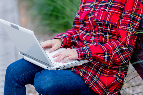 Νεαρή γυναίκα που εργάζεται χρησιμοποιώντας σημειωματάριο έξω κάθεται σε παγκάκι. - Φωτογραφία, εικόνα