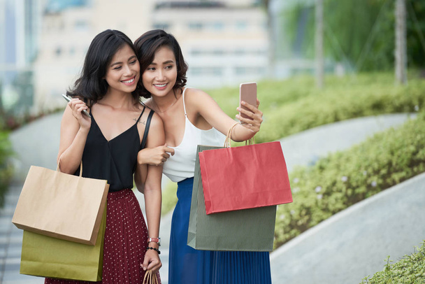 Attrayant jeunes femmes asiatiques avec des sacs à provisions prenant selfie ensemble
 - Photo, image