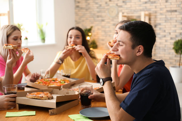 Young people eating pizza at table indoors - Foto, afbeelding