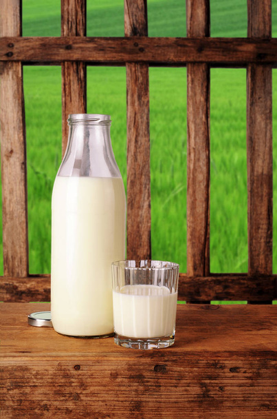 Milchflasche und Glas mit Milch, Holzzaun - Foto, Bild