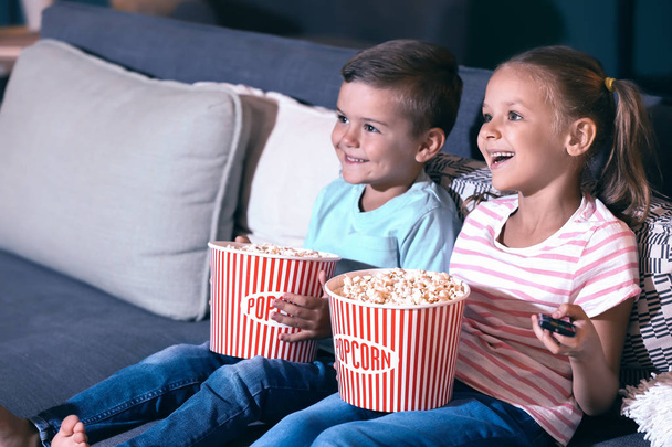Children eating popcorn while watching TV in evening - Foto, afbeelding