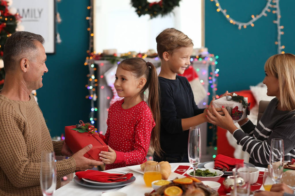 Счастливая семья дарить друг другу подарки во время рождественского ужина дома
 - Фото, изображение