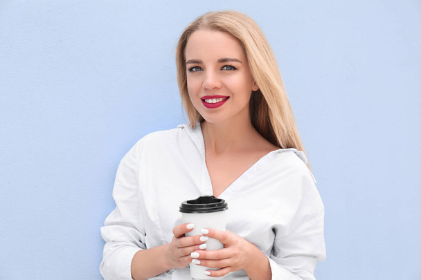 Όμορφη νεαρή γυναίκα με φλιτζάνι καφέ κοντά στον τοίχο χρώμα - Φωτογραφία, εικόνα