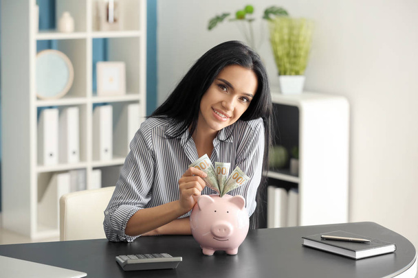 Young woman with piggy bank sitting at table - Foto, Imagem