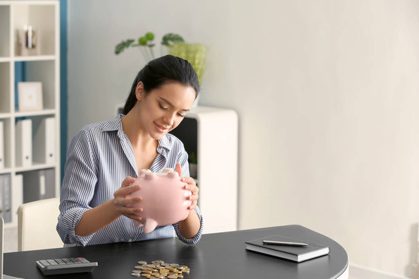 Jovem mulher derrubando dinheiro do banco porquinho enquanto sentado à mesa
 - Foto, Imagem