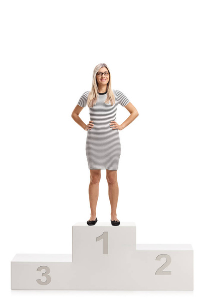 Full length portrait of a young woman standing on a winners pedestal and smiling isolated on white background - Foto, afbeelding