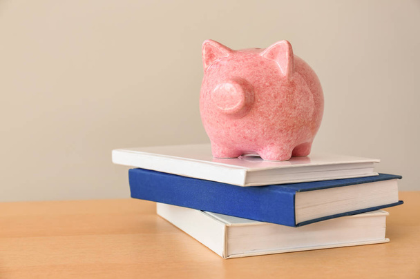 Piggy bank and stack of books on light wooden table - Photo, Image
