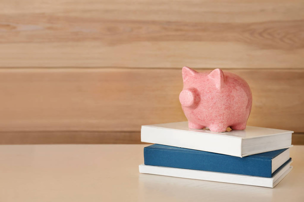 Cute piggy bank with books on light wooden table - Photo, Image