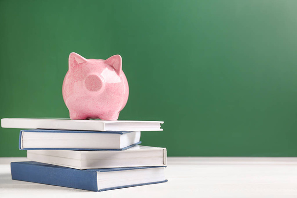 Cute piggy bank on stack of books against color background - Photo, Image