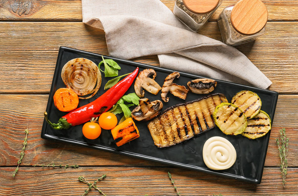 Тарелка с вкусными овощами на гриле и соусом на деревянном столе
 - Фото, изображение