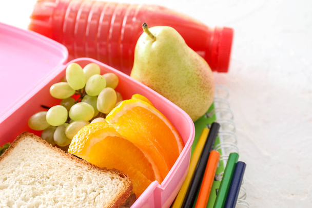 Lunchbox mit appetitlichen Speisen und Schreibwaren auf hellem Tisch - Foto, Bild